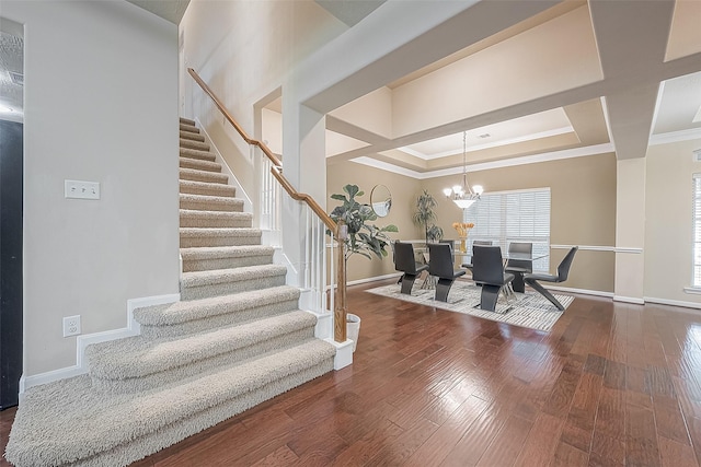 stairway featuring crown molding, a raised ceiling, an inviting chandelier, and wood-type flooring