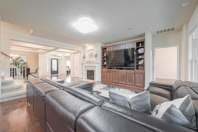 living room featuring a tiled fireplace, a textured ceiling, a chandelier, and hardwood / wood-style flooring