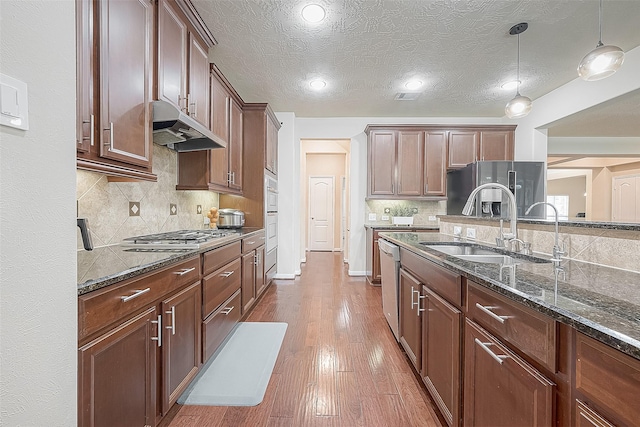 kitchen featuring dark stone countertops, pendant lighting, stainless steel appliances, and sink