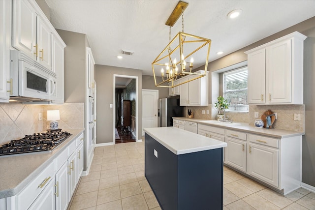 kitchen with stainless steel appliances, decorative light fixtures, a kitchen island, sink, and white cabinets