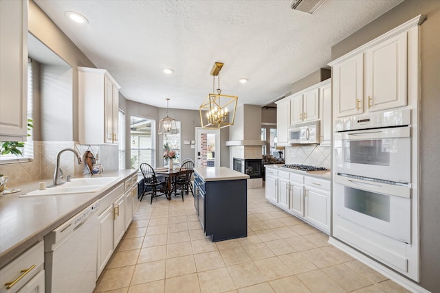 kitchen with white cabinetry, decorative light fixtures, a kitchen island, sink, and white appliances