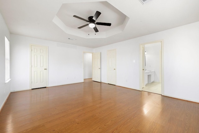 unfurnished bedroom featuring a tray ceiling, hardwood / wood-style flooring, ceiling fan, and ensuite bath