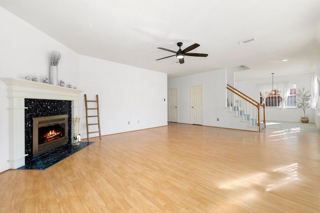 unfurnished living room with a high end fireplace, light hardwood / wood-style floors, and ceiling fan with notable chandelier