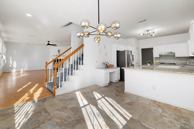 kitchen with light stone counters, pendant lighting, stainless steel refrigerator, backsplash, and white cabinetry