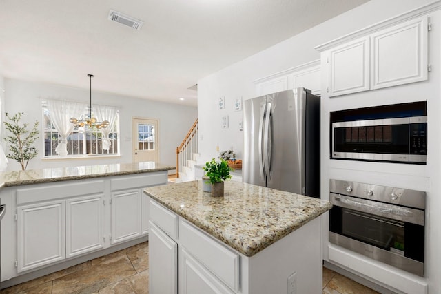 kitchen featuring light stone counters, white cabinetry, a kitchen island, stainless steel appliances, and hanging light fixtures