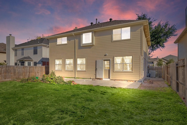 back house at dusk with a patio and a lawn