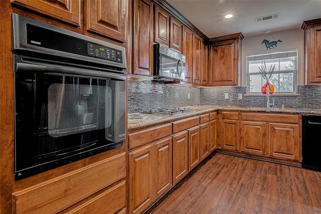 kitchen featuring sink, hardwood / wood-style flooring, black appliances, and tasteful backsplash