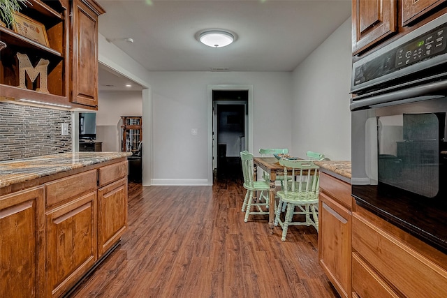 kitchen featuring black oven, tasteful backsplash, stone countertops, and dark hardwood / wood-style flooring