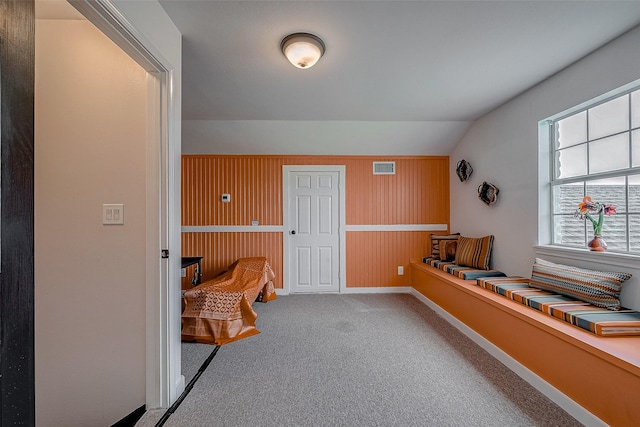 interior space with vaulted ceiling, carpet, and wood walls