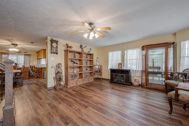 sitting room with a textured ceiling, a fireplace, wood finished floors, a ceiling fan, and baseboards