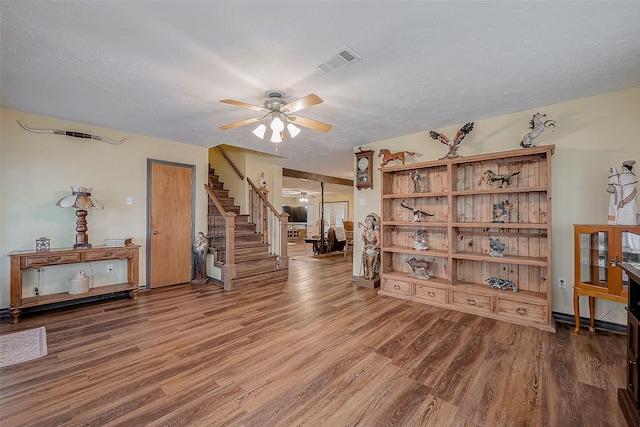 sitting room with stairs, ceiling fan, wood finished floors, and visible vents