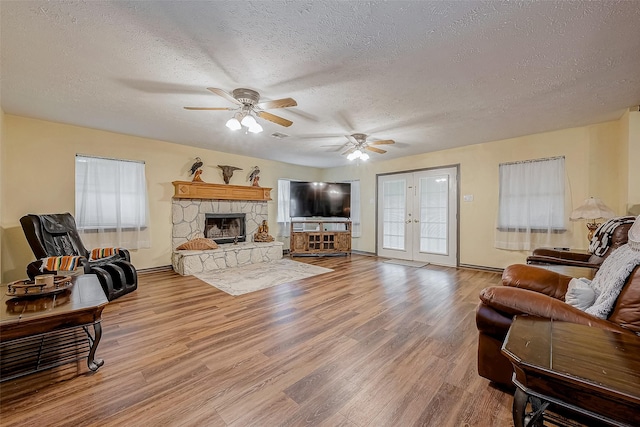 living room with ceiling fan, wood finished floors, a textured ceiling, french doors, and a fireplace