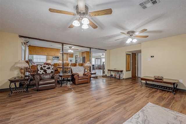 living room with light wood-type flooring, a ceiling fan, visible vents, and a textured ceiling