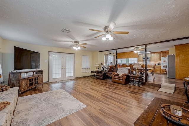 living area featuring french doors, visible vents, light wood-style flooring, ceiling fan, and a textured ceiling