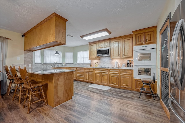 kitchen featuring a peninsula, wood finished floors, appliances with stainless steel finishes, brown cabinetry, and a kitchen bar