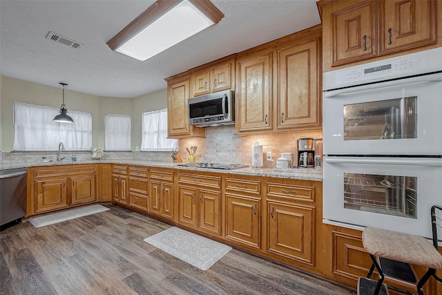 kitchen featuring a sink, visible vents, appliances with stainless steel finishes, light stone countertops, and pendant lighting