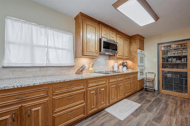 kitchen featuring appliances with stainless steel finishes, brown cabinetry, dark wood-type flooring, and light stone countertops