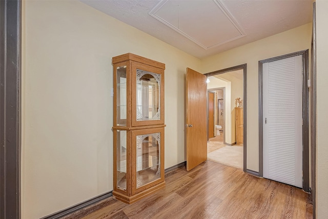 hall with light wood-type flooring, attic access, and baseboards