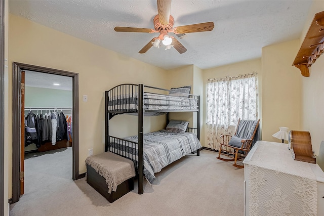 bedroom with a walk in closet, a closet, light carpet, and a textured ceiling