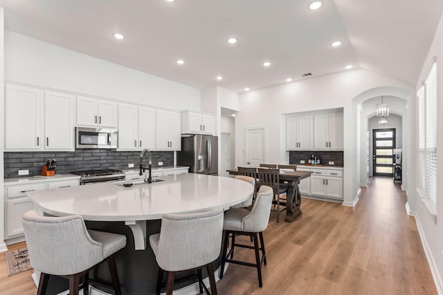 kitchen with stainless steel appliances, white cabinets, and an island with sink