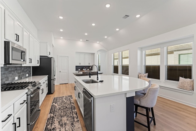 kitchen featuring stainless steel appliances, a sink, white cabinetry, light countertops, and an island with sink