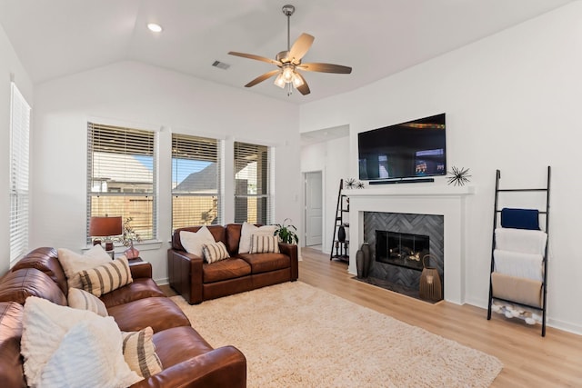 living area with a fireplace, lofted ceiling, visible vents, a ceiling fan, and wood finished floors