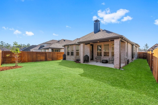 rear view of property with a fenced backyard, brick siding, a yard, a chimney, and a patio area