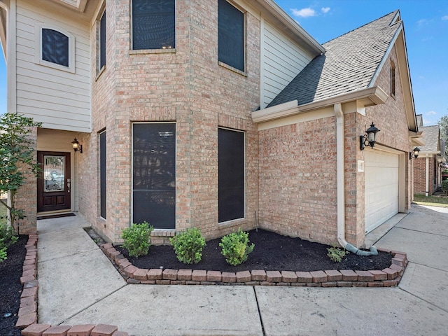 view of front facade with brick siding, an attached garage, driveway, and roof with shingles