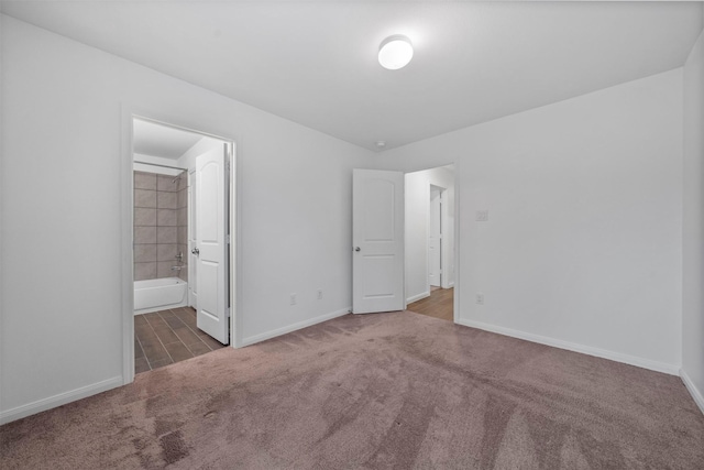 unfurnished bedroom with ensuite bathroom and dark colored carpet