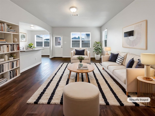 living area featuring arched walkways, dark wood-type flooring, visible vents, and a healthy amount of sunlight