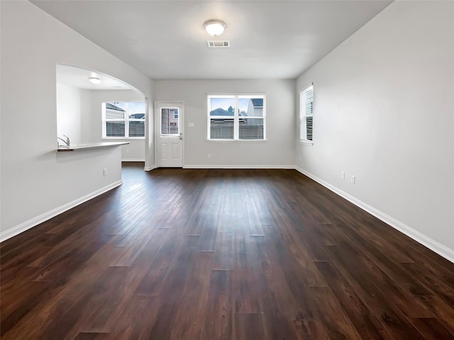 unfurnished living room featuring dark wood-style floors, baseboards, visible vents, and a healthy amount of sunlight