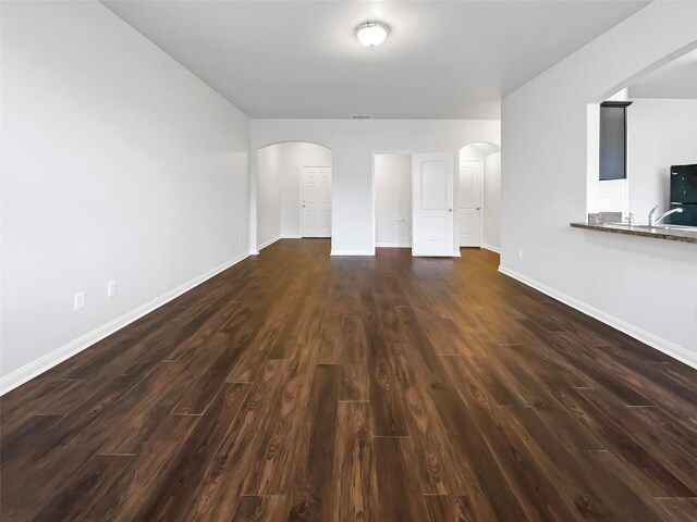 unfurnished living room with dark wood-type flooring, arched walkways, and baseboards