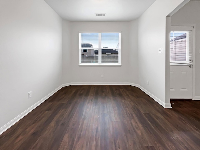 spare room featuring dark wood-style flooring, visible vents, and baseboards