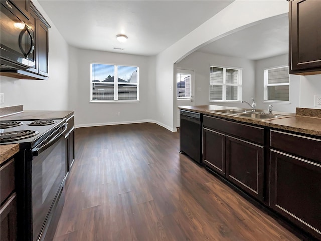 kitchen with arched walkways, a sink, dark brown cabinets, black appliances, and dark countertops