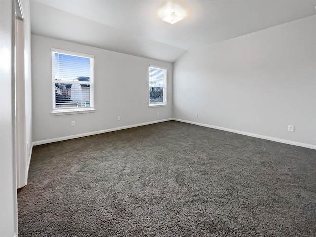 empty room featuring lofted ceiling, dark carpet, and baseboards