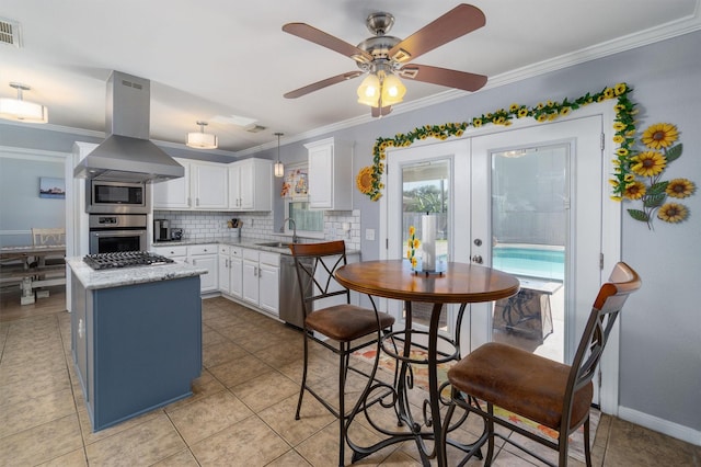 kitchen with stainless steel appliances, island range hood, backsplash, ornamental molding, and white cabinetry