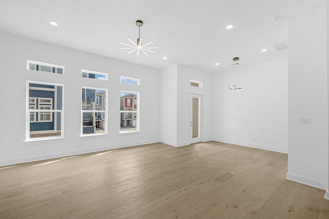 unfurnished living room featuring a notable chandelier and light hardwood / wood-style flooring