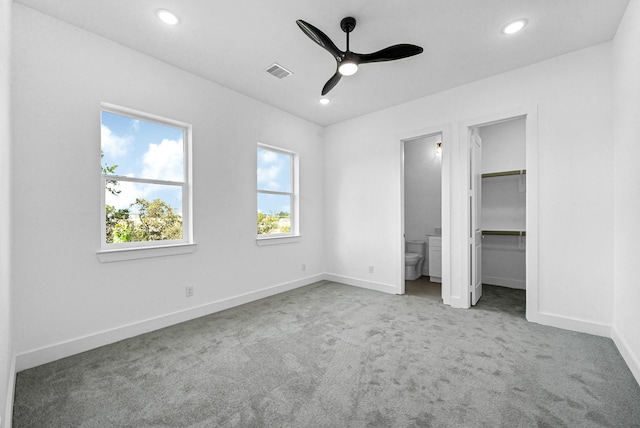 unfurnished bedroom featuring ceiling fan, a spacious closet, light colored carpet, and ensuite bathroom