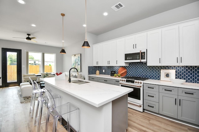 kitchen featuring a center island with sink, white appliances, light stone countertops, decorative light fixtures, and sink