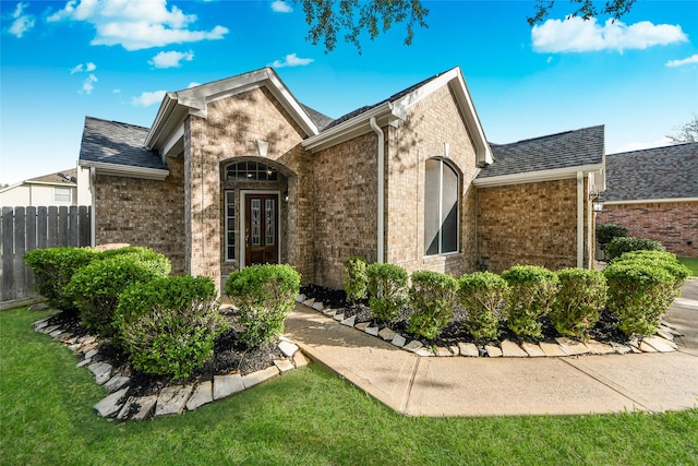 view of front of home with a shingled roof, fence, a front lawn, and brick siding