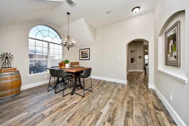 dining space with arched walkways, visible vents, vaulted ceiling, wood finished floors, and baseboards