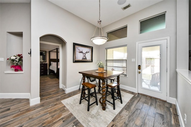 dining room featuring arched walkways, dark wood-type flooring, visible vents, and baseboards