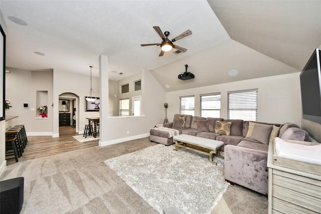 living area featuring carpet floors, arched walkways, vaulted ceiling, ceiling fan, and baseboards