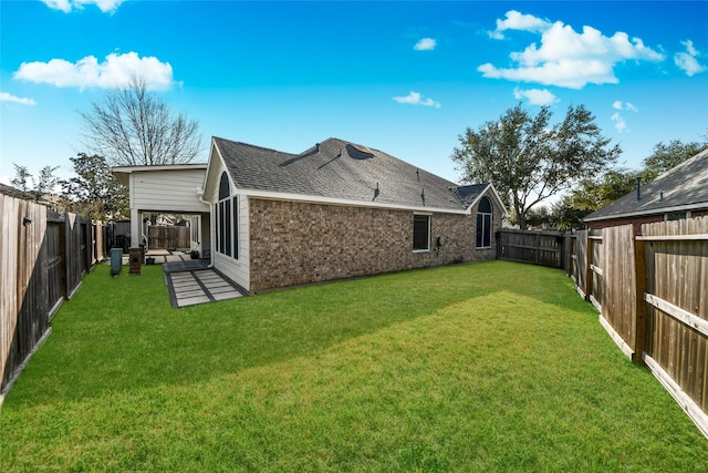 back of property with roof with shingles, brick siding, a lawn, and a fenced backyard