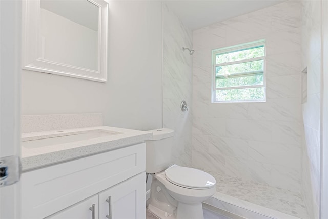 bathroom with toilet, tiled shower, and vanity