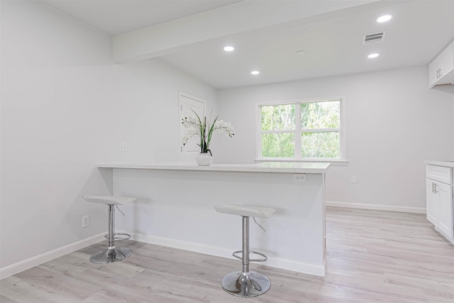 interior space featuring light hardwood / wood-style flooring, kitchen peninsula, a breakfast bar, and white cabinets