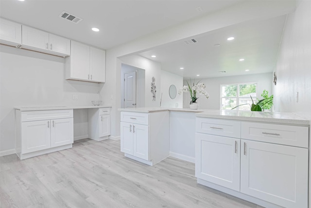 kitchen featuring light wood-type flooring, kitchen peninsula, built in desk, and white cabinets