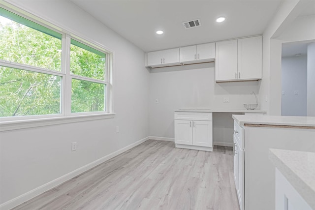 kitchen with light hardwood / wood-style flooring, built in desk, and white cabinets