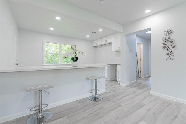 kitchen with kitchen peninsula, light hardwood / wood-style floors, white cabinetry, and a breakfast bar area