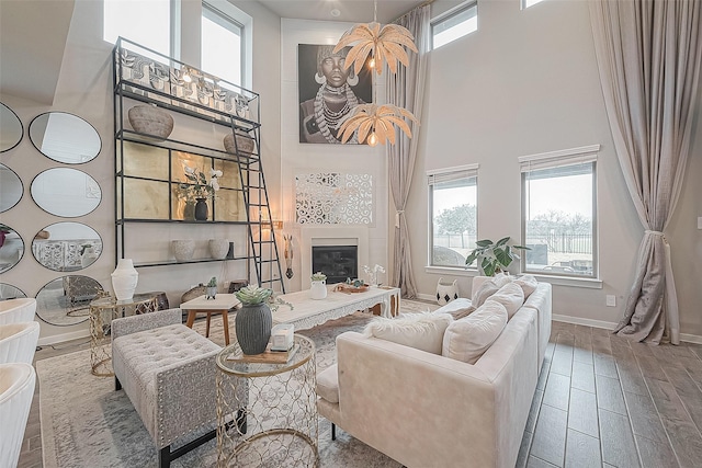 living room featuring a healthy amount of sunlight, wood-type flooring, a large fireplace, and a towering ceiling